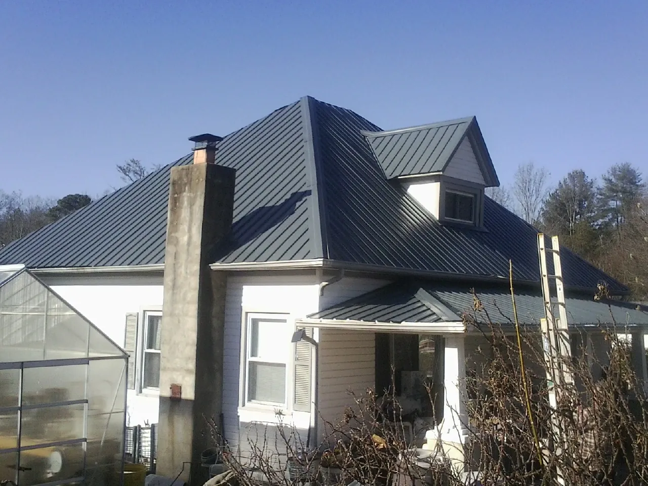 Dark blue standing seam metal roof on a white farmhouse with dormer — Slate & Tile Roof Repair by Roofing Brothers in Seagoville