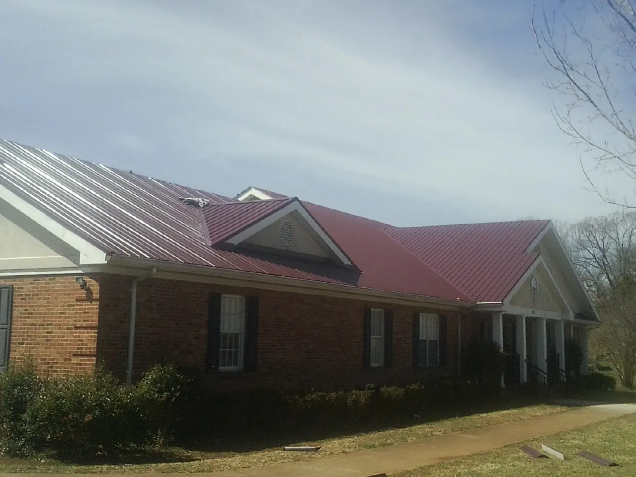 Red metal roof with gabled entries on a long brick building, from a Hail Damage Roof Repair job in Seagoville