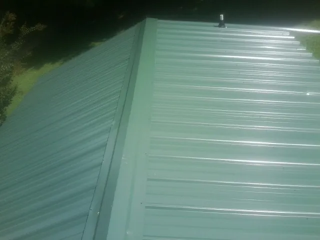 New green metal panels meeting at the ridge of a roof — Flat Roof Repair work by our crew in Seagoville