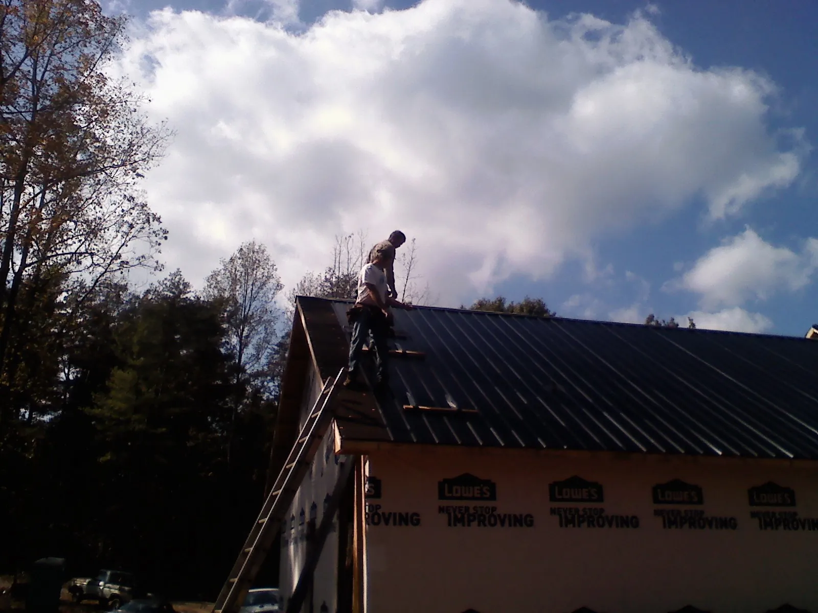 Roofer fastening dark metal panels high against a cloudy sky, from a Roof Inspection job in Seagoville