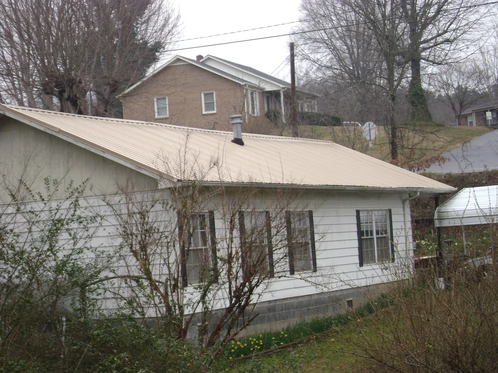 Tan metal roof on a white sided house set into a hillside — Commercial Roofing by Roofing Brothers in Seagoville