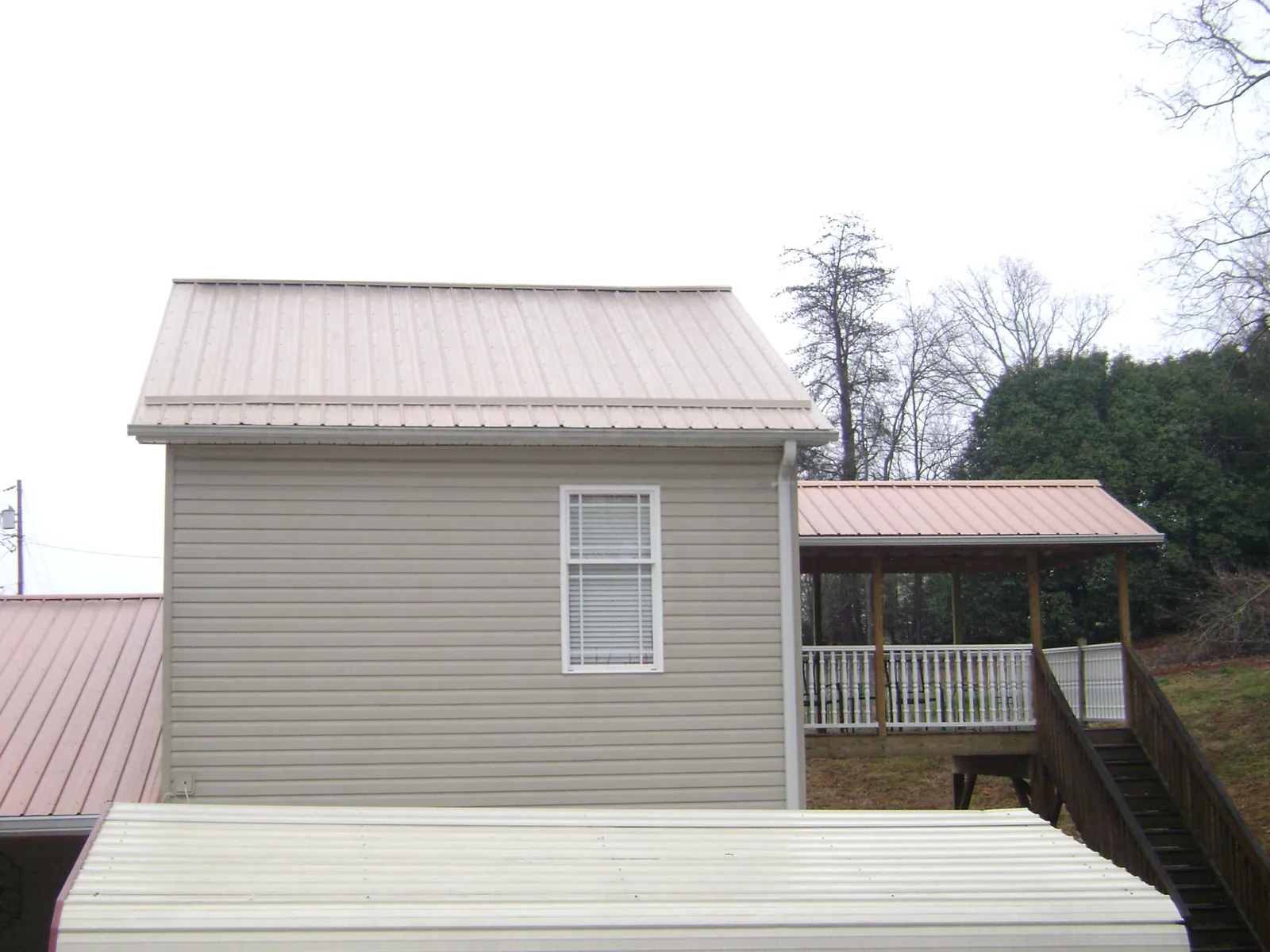 Tan metal roofs on a two story addition and attached porch, from a Roof Replacement job in Seagoville